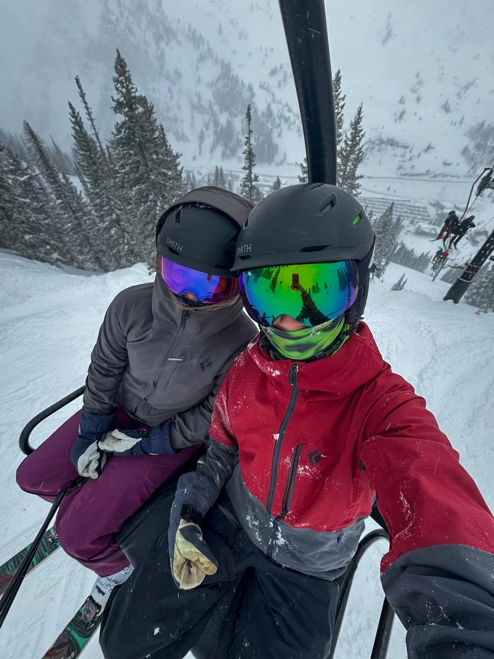 Two skiers in helmets and goggles on a snowy chairlift