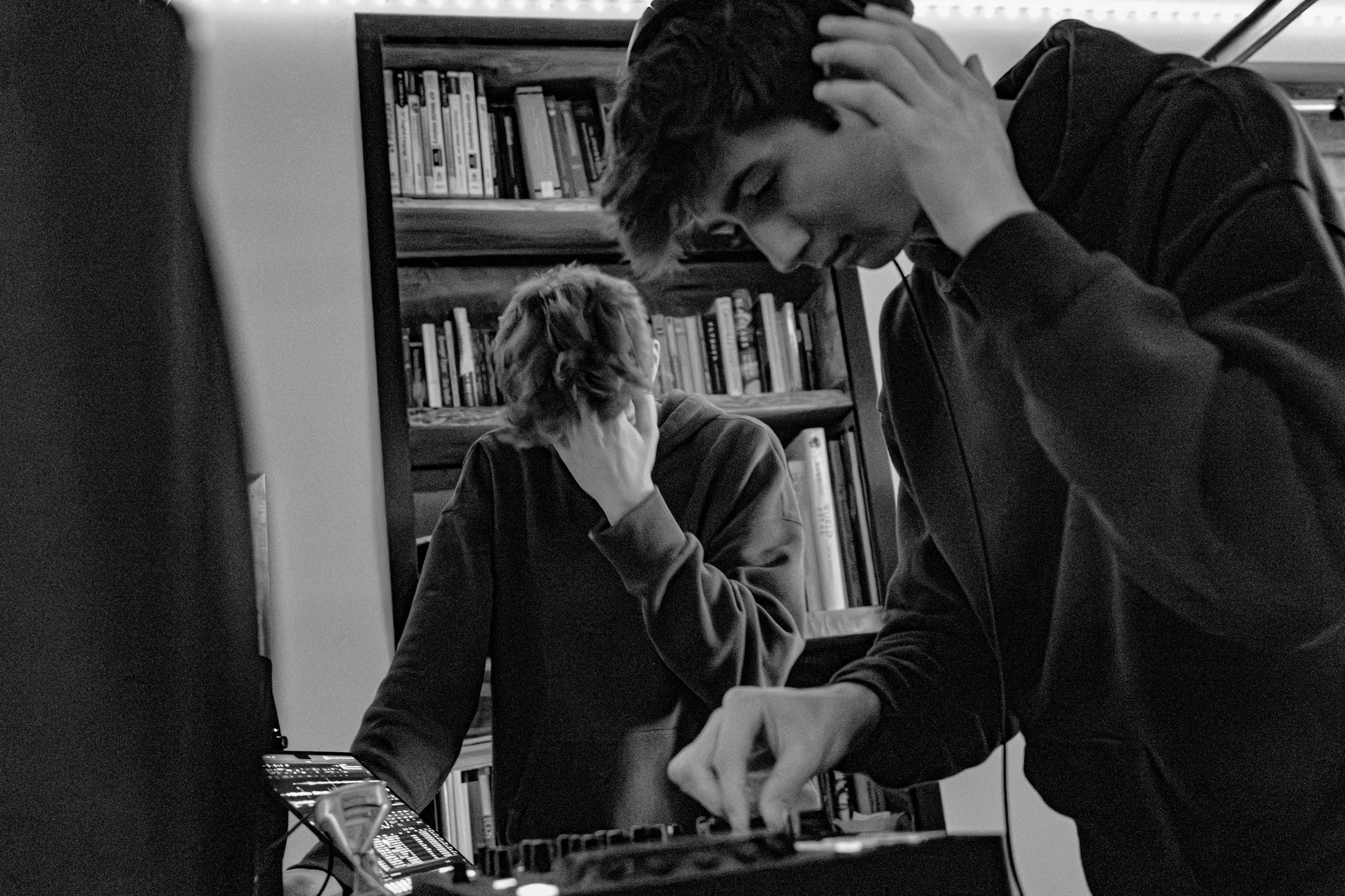 Judah at the decks in front of a wall of books, one hand on his headphones