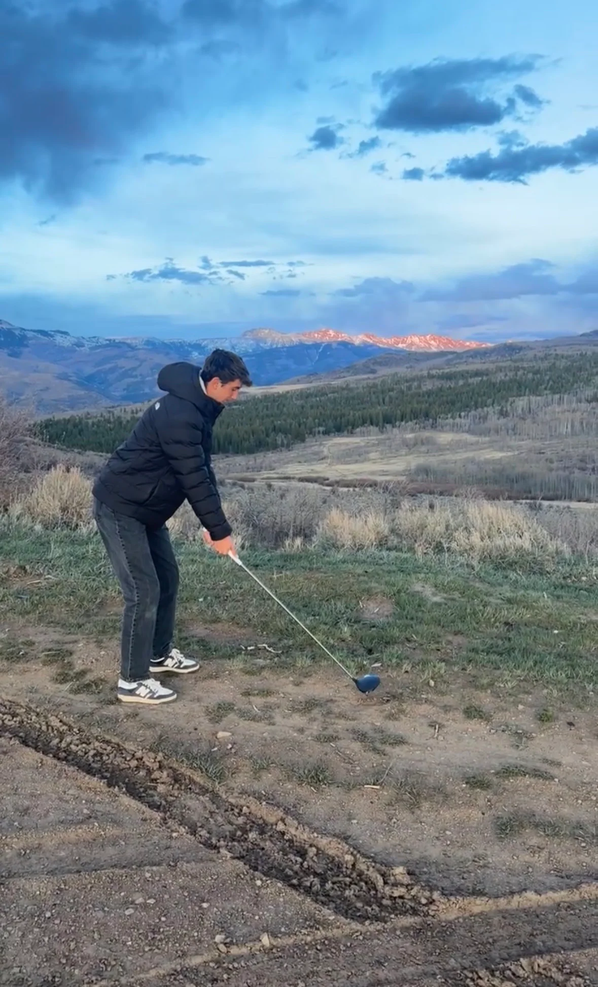 Judah driving a golf ball toward alpenglow on the mountain horizon