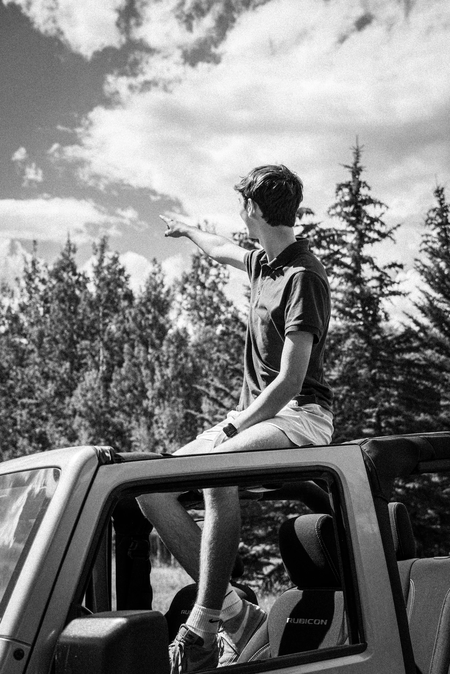 Judah sitting on the roof of his Jeep, pointing toward the treeline