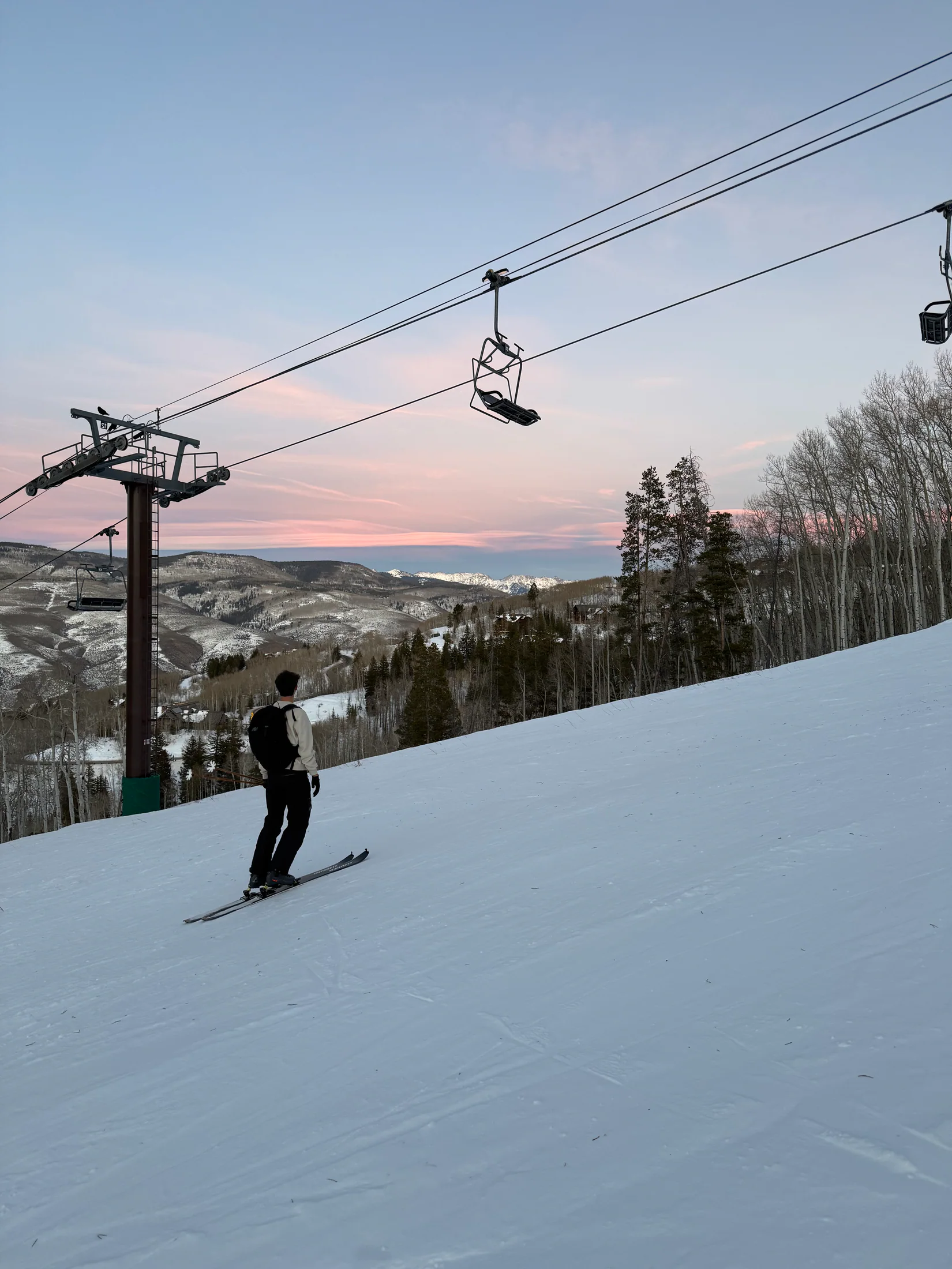 A lone skier gliding beneath the chairlift as the sky turns pink at dusk
